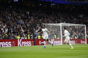 Vinícius Júnior corriendo con los brazos abiertos para celebrar un gol cerca de la portería en el Santiago Bernabéu.