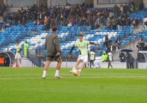 Un jugador del Real Madrid Castilla golpeando el balón durante los ejercicios de calentamiento previos bajo la lluvia.