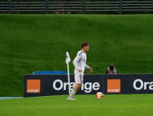 Jugador del Real Madrid Castilla controlando el balón cerca del banderín de córner en un partido lluvioso.