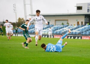 El delantero del Real Madrid Castilla (dorsal 3) saltando para esquivar la salida del portero Mestre en el área chica.