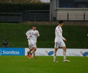 Jugadores del Real Madrid Castilla corriendo sobre el césped mojado durante un partido bajo la lluvia en Valdebebas.